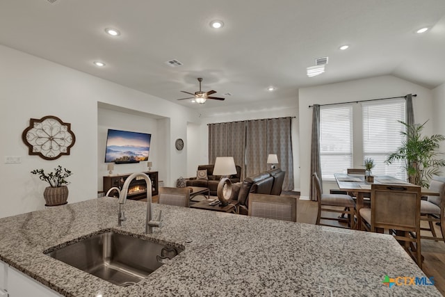 kitchen featuring dark hardwood / wood-style flooring, lofted ceiling, light stone counters, sink, and ceiling fan