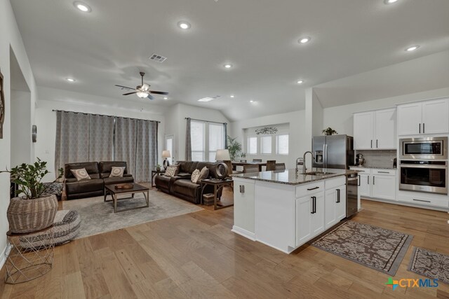 kitchen with dark stone counters, appliances with stainless steel finishes, a center island with sink, and white cabinets