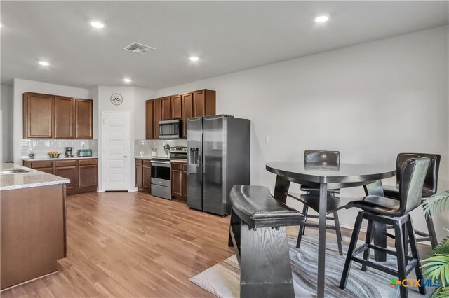 kitchen with sink, light stone counters, appliances with stainless steel finishes, tasteful backsplash, and light wood-type flooring