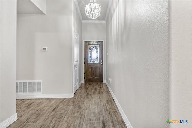 entryway with hardwood / wood-style flooring, ornamental molding, and an inviting chandelier