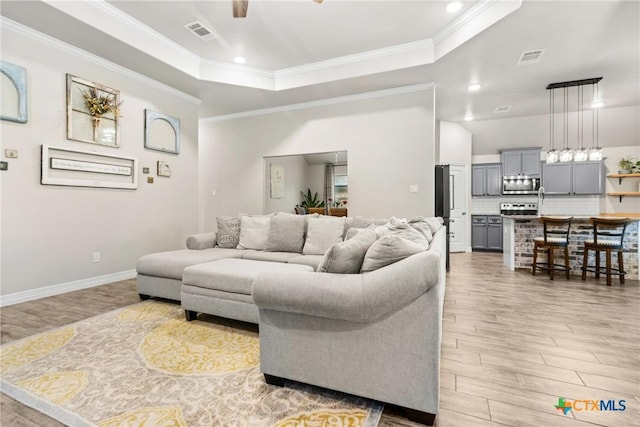 living room with a tray ceiling, ornamental molding, and light wood-type flooring