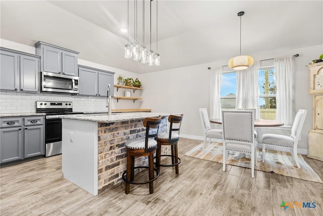 kitchen featuring decorative light fixtures, stainless steel appliances, and an island with sink