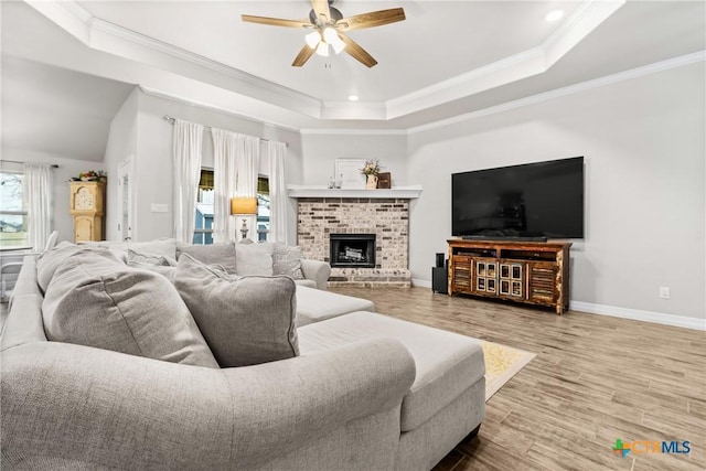 living room featuring crown molding, hardwood / wood-style flooring, ceiling fan, a tray ceiling, and a brick fireplace