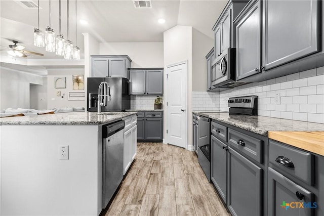 kitchen with gray cabinets, pendant lighting, wood counters, tasteful backsplash, and stainless steel appliances