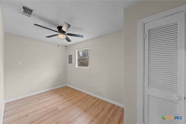 empty room featuring a ceiling fan, baseboards, visible vents, light wood-style floors, and electric panel