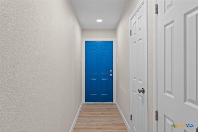 doorway to outside featuring a textured wall, light wood-style flooring, and baseboards