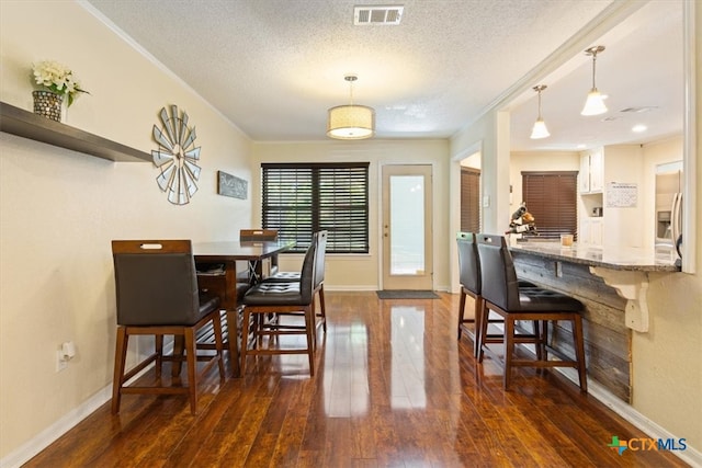 dining area with a textured ceiling, ornamental molding, and dark wood-type flooring