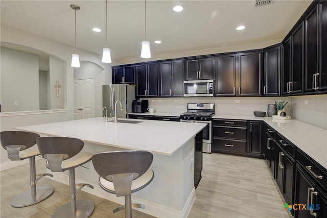 kitchen featuring sink, pendant lighting, stainless steel appliances, and an island with sink