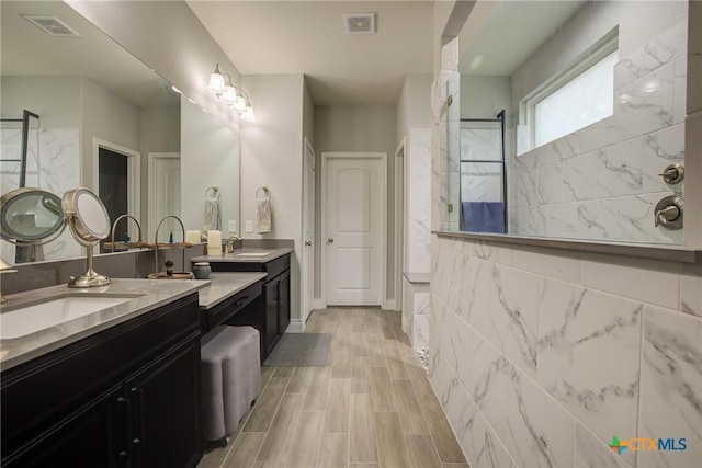 bathroom with tiled shower, vanity, and tile walls