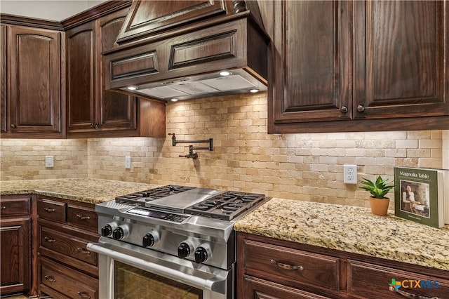 kitchen featuring dark brown cabinetry, light stone counters, stainless steel stove, premium range hood, and decorative backsplash