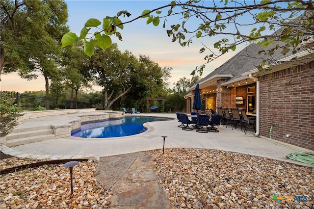 pool at dusk featuring a patio