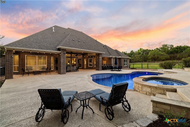 pool at dusk with a patio and an in ground hot tub