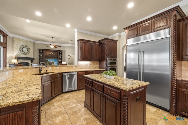 kitchen with ornamental molding, a stone fireplace, a kitchen island, appliances with stainless steel finishes, and sink