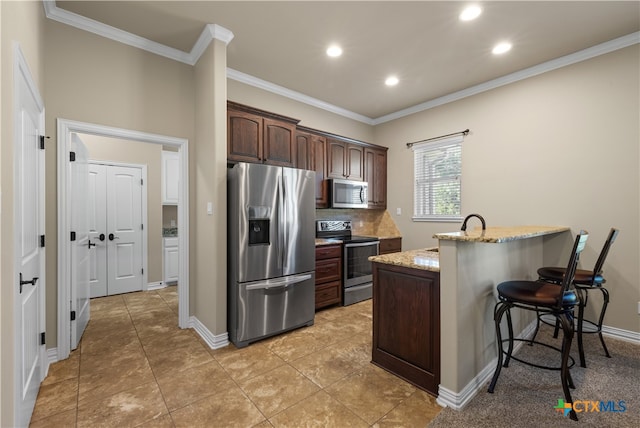 kitchen with stainless steel appliances, a center island with sink, light stone counters, a breakfast bar area, and dark brown cabinets