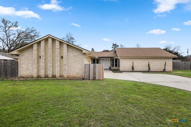 view of front of house with driveway, stone siding, fence, and a front lawn