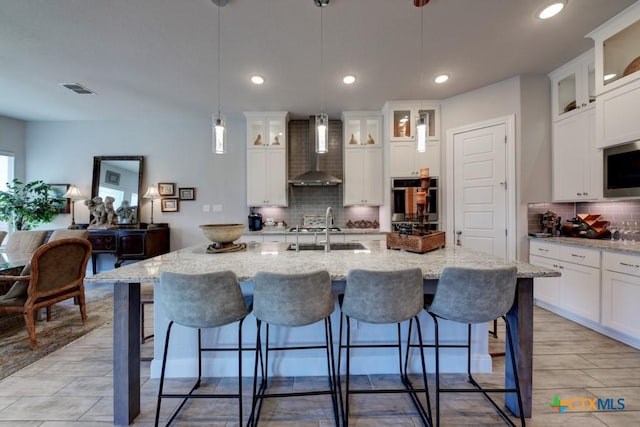 kitchen with sink, hanging light fixtures, stainless steel appliances, a center island with sink, and wall chimney exhaust hood