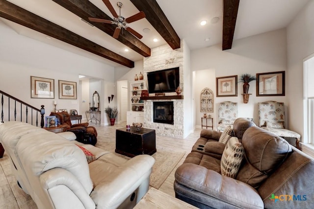 living room with ceiling fan, a stone fireplace, and beam ceiling