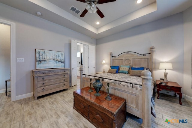 bedroom featuring light hardwood / wood-style flooring, a raised ceiling, and ceiling fan