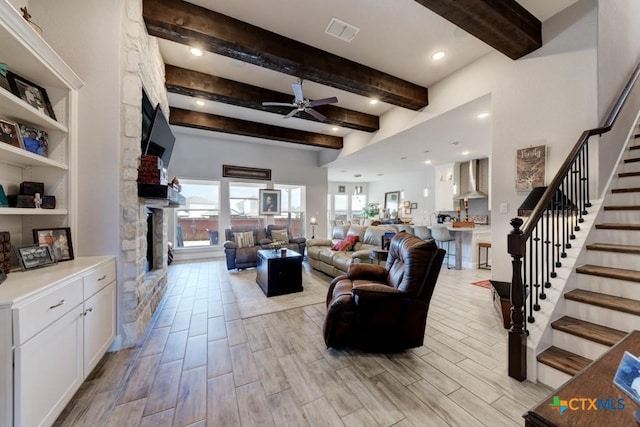 living room with a stone fireplace, beamed ceiling, and ceiling fan