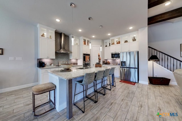 kitchen featuring an island with sink, white cabinetry, sink, stainless steel appliances, and wall chimney range hood