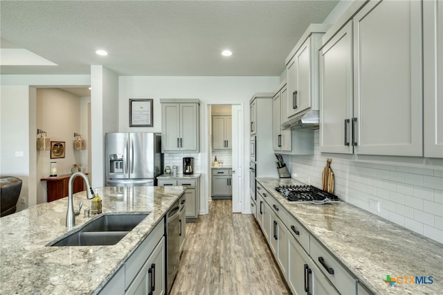 19500 Chayton Cir, Pflugerville, TX 78660 - kitchen featuring appliances with stainless steel finishes, a sink, under cabinet range hood, light stone counters, and light wood-style flooring