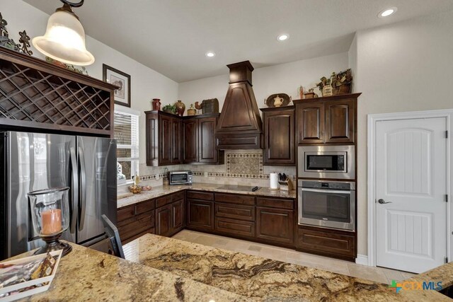 108 Westfield Vw, La Vernia, TX 78121 - kitchen featuring stainless steel appliances, backsplash, dark brown cabinetry, light stone countertops, and custom exhaust hood