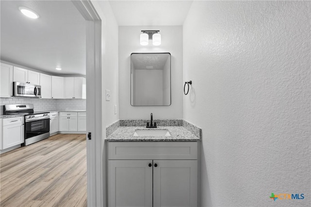 bathroom with a textured wall, decorative backsplash, a sink, and wood finished floors