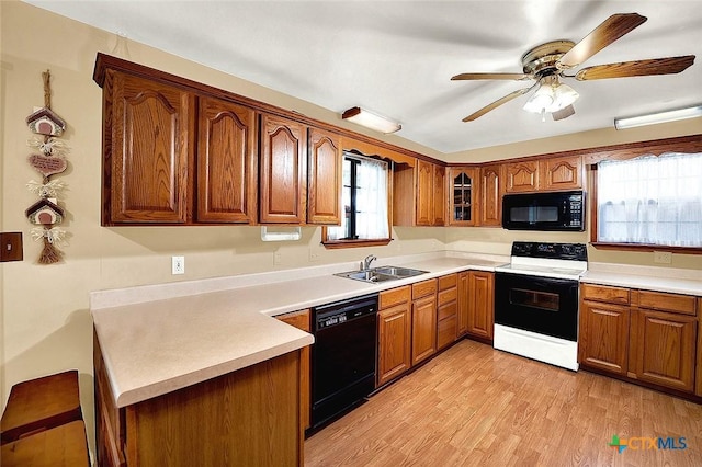 kitchen with a sink, light countertops, brown cabinets, black appliances, and glass insert cabinets