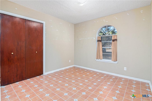 unfurnished bedroom featuring a closet, a textured ceiling, and light tile patterned flooring