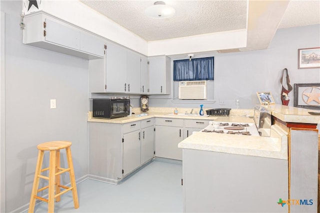 kitchen featuring a breakfast bar, cooling unit, gray cabinetry, a textured ceiling, and kitchen peninsula