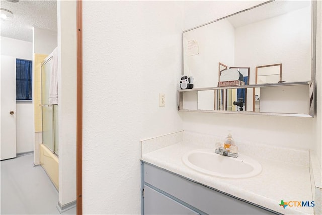 bathroom featuring bath / shower combo with glass door, vanity, and a textured ceiling