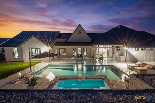 pool at dusk with an in ground hot tub and a patio