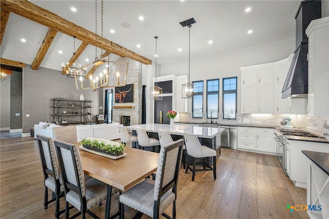 dining room with sink, beam ceiling, high vaulted ceiling, a fireplace, and light hardwood / wood-style floors