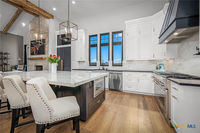 kitchen with appliances with stainless steel finishes, white cabinetry, hanging light fixtures, a center island, and custom range hood