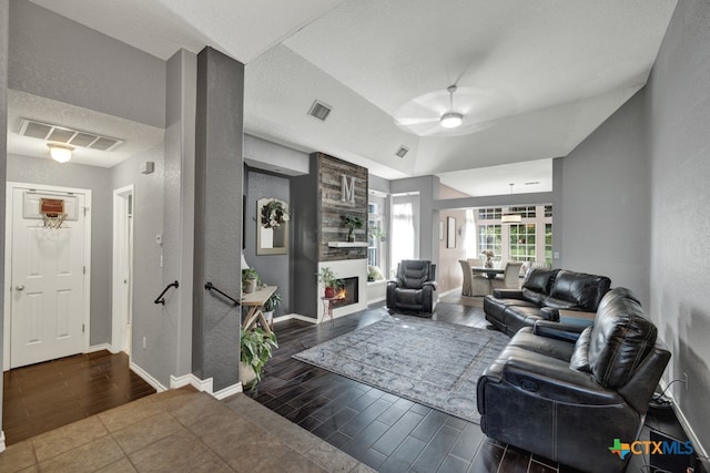 living room with a textured ceiling, dark hardwood / wood-style flooring, vaulted ceiling, a large fireplace, and ceiling fan