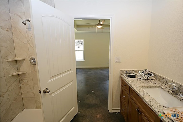 full bath with a ceiling fan, a tile shower, vanity, and baseboards