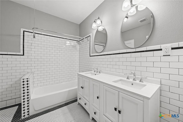 bathroom with tile walls, tile patterned flooring, tiled shower / bath combo, and vanity