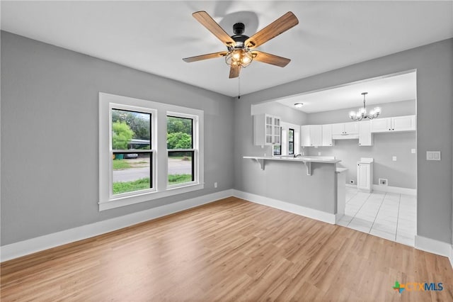 unfurnished living room featuring ceiling fan with notable chandelier and light hardwood / wood-style flooring