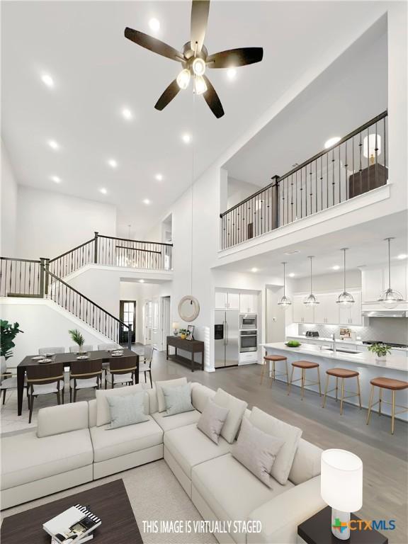 living area featuring stairs, a high ceiling, ceiling fan, and recessed lighting