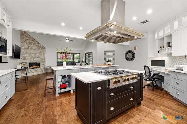 kitchen featuring stainless steel appliances, island range hood, vaulted ceiling, white cabinets, and a kitchen island