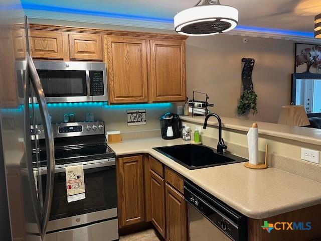 730 E Mather St Unit K203, New Braunfels, TX 78130 - kitchen with stainless steel appliances, a peninsula, ornamental molding, brown cabinetry, and light countertops