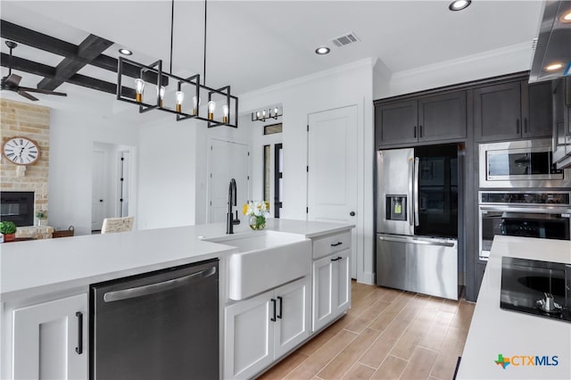 kitchen featuring sink, a stone fireplace, light hardwood / wood-style floors, white cabinets, and appliances with stainless steel finishes