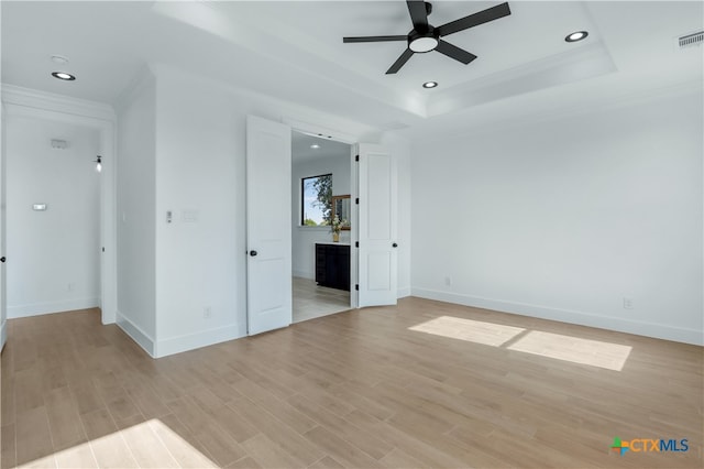 spare room featuring ceiling fan, light wood-type flooring, and a tray ceiling