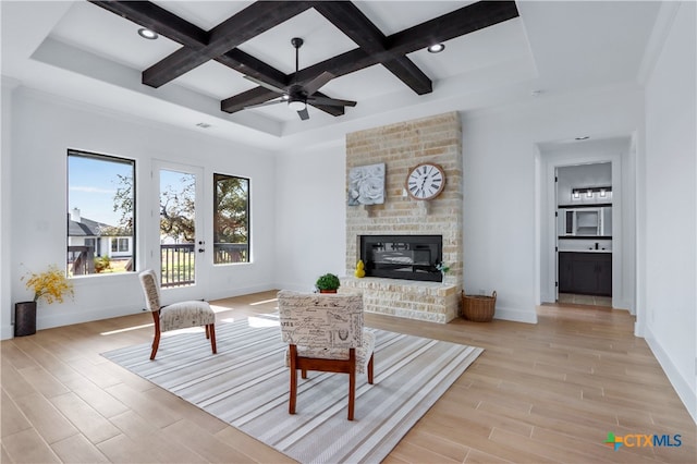 living room featuring ceiling fan, light hardwood / wood-style floors, a fireplace, and coffered ceiling