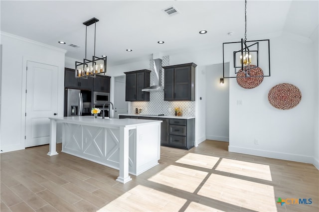 kitchen with appliances with stainless steel finishes, a breakfast bar, wall chimney range hood, a center island with sink, and light hardwood / wood-style flooring