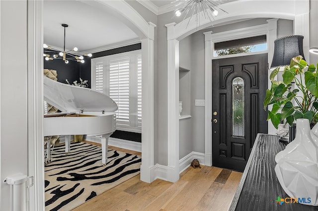 foyer with an inviting chandelier, wood-type flooring, and crown molding