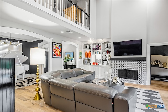 living room with a high ceiling, ornamental molding, a fireplace, light hardwood / wood-style flooring, and a notable chandelier