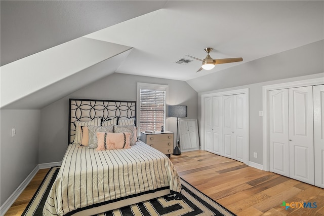 bedroom with two closets, ceiling fan, light wood-type flooring, and vaulted ceiling