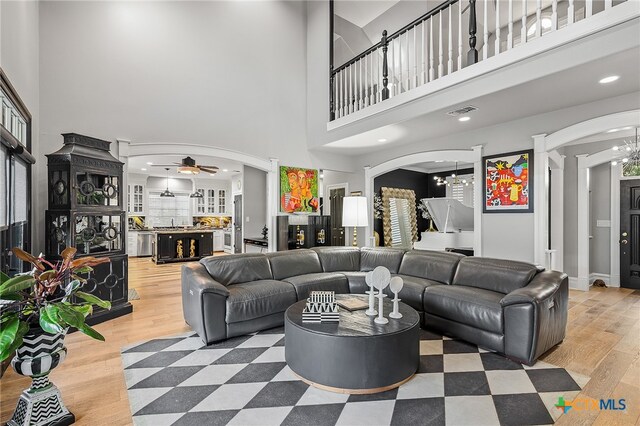 living room with hardwood / wood-style floors, a high ceiling, and ceiling fan with notable chandelier