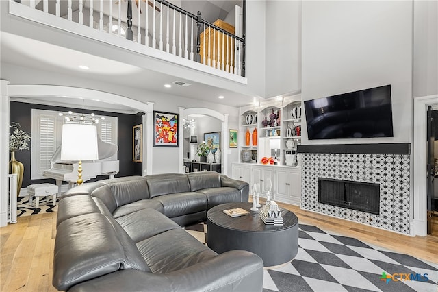 living room with a towering ceiling, a tiled fireplace, wood-type flooring, and an inviting chandelier